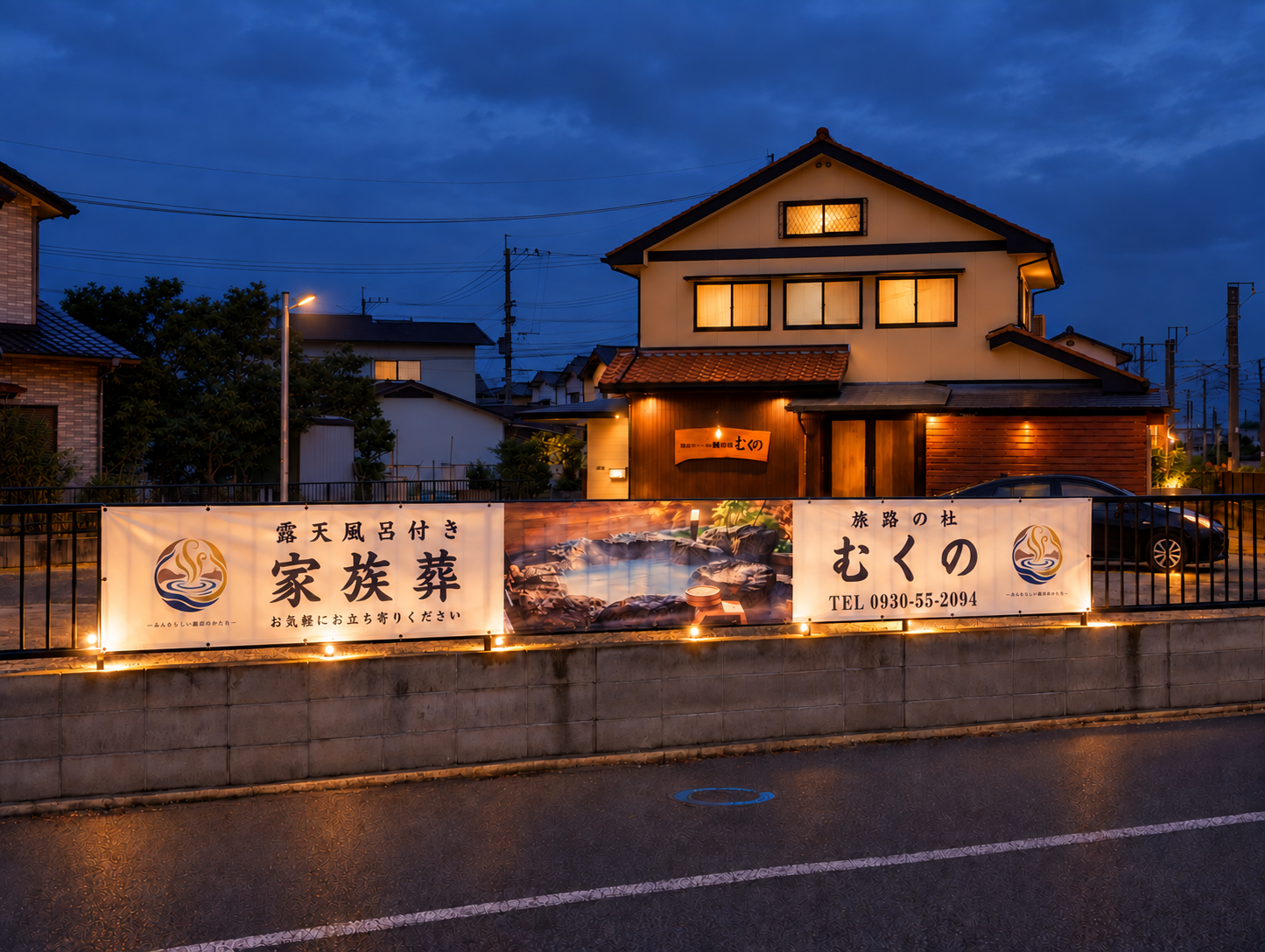 露天風呂付き家族葬　旅路の杜むくの 外観。夕暮れに暖かな照明が灯る建物と横断幕